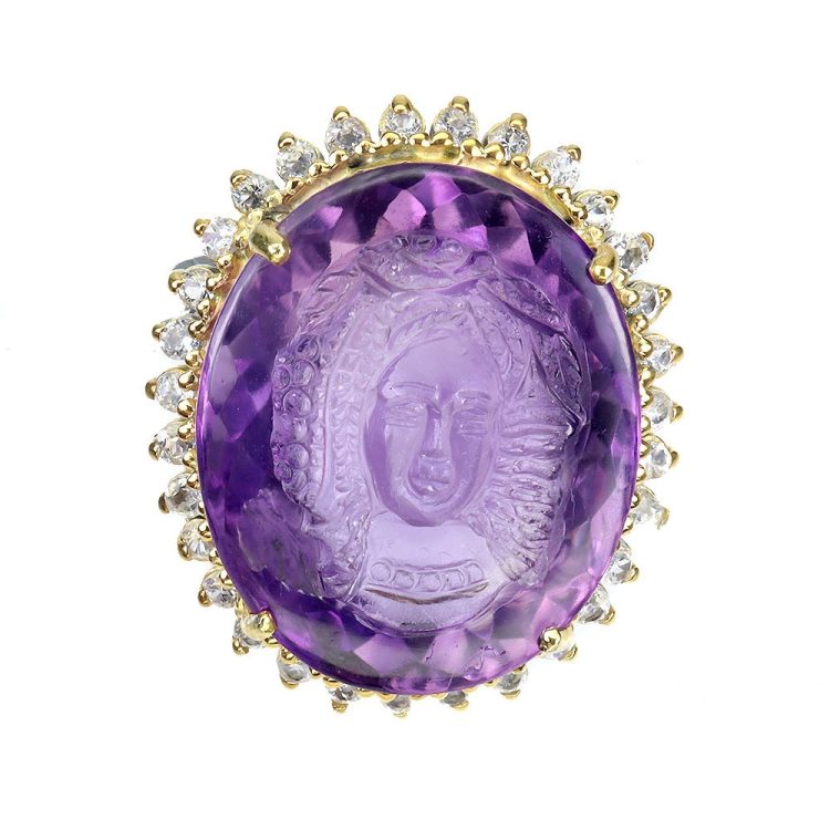 Καρφίτσα/Μενταγιόν σε ασήμι 925 με λευκό και κίτρινο επιχρύσωμα στα 14Κ μια καρφίτσα/μενταγιον Καμέο με ένα σκαλισμένο στο χέρι Αμέθυστο σε Oval κοπή με transparent καθαρότητα διαφάνεια στα 37.88 ct βάρος και έντονο μοβ χρώμα. Το κόσμημα περιέχει και 33 λευκά Τοπάζια σε round με Vvs καθαρότητα. Η προέλευση των λίθων είναι απο την Βραζιλία.