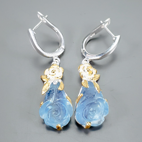 Σκουλαρίκια σε ασήμι 925 με λευκό και κίτρινο επιχρύσωμα στα 14Κ με δύο σκαλιστές Ακουαμαρίνες σκαλισμένη σε μορφή Κρίνων με transparent καθαρότητα στα 26.38 ct με έντονο γαλάζιο χρώμα. Η προέλευση των λίθων είναι απο την Βραζιλία.