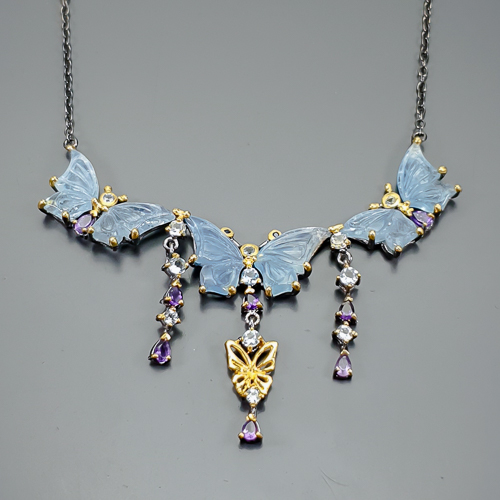Χειροποίητο κολιέ σε ασήμι 925 με μαύρο και κίτρινο επιχρύσωμα στα 14Κ με έξη σκαλιστές Ακουαμαρίνες σε κοπές hand carved fancy,και 12 Round στα 99.17 ct συνολικό βάρος με transparent & Vvs διαφάνεια καθαρότητα και έντονο γαλάζιο χρώμα. Στο κέντρο του κολιέ το μοτιφ αναπαριστά τρεις πανέμορφες πεταλούδες που τα φτερά τους αποτελούνται από δυο σκαλιστές ακουαμαρίνες και έχουμε στις κεραίες τους από δυο φυσικά Μπλε Ζαφείρια σε στρογγυλή κοπή με βαθύ μπλε χρώμα και συνολικό βάρος 0.12 ct και opaque διαφάνεια καθαρότητα, στο σώμα κάθε πεταλούδας υπάρχουν και 8 Αμέθυστοι σε κοπή σταγόνας με συνολικό βάρος 4.80 ct με Vvs διαφάνεια. Η προέλευση των λίθων είναι από την Βραζιλία και την Μοζαμβίκη .