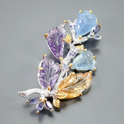 Καρφίτσα σε ασήμι 925 με λευκό και κίτρινο επιχρύσωμα στα 14Κ με δύο σκαλιστούς Αμέθυστους σε σχήμα Φύλλου με If καθαρότητα διαφάνεια στα 20.10 ct βάρος και έντονο μοβ χρώμα. Το κόσμημα περιέχει και δύο σκαλιστές Ακουαμαρίνες σκαλισμένη σε μορφή Κρίνων με transparent καθαρότητα στα 17.35 ct με έντονο γαλάζιο χρώμα, Ένα Κιτρίνη Χαλαζία σκαλιστό σε σχήμα φύλλου με if-Vvs καθαρότητα και βάρος 15.33 ct και τέλος το κόσμημα συμπληρώνουν και 6 Ιολίτες σε marquise  κοπή με vvs διαφάνεια καθαρότητα και συνολικό βάρος 3.00 ct. Η προέλευση των λίθων είναι απο την Βραζιλία.