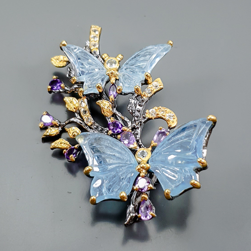 Χειροποίητη καρφίτσα σε ασήμι 925 με μαύρο και κίτρινο επιχρύσωμα στα 14Κ με τέσσερις σκαλιστές Ακουαμαρίνες σε κοπές hand carved fancy,και 2 Round στα 28.60 ct συνολικό βάρος με transparent & Vvs διαφάνεια καθαρότητα και έντονο γαλάζιο χρώμα. Στο κέντρο του κολιέ το μοτιφ αναπαριστά ένα ανοιξιάτικο τοπίο με δυο πανέμορφες πεταλούδες που τα φτερά τους αποτελούνται από δυο σκαλιστές ακουαμαρίνες και έχουμε στις κεραίες τους άλλα και στο υπόλοιπο μοτιφ από Αμέθυστους σε Pear κοπή με υπέροχο μοβ χρώμα και συνολικό βάρος 4.50 ct και If-vvs διαφάνεια καθαρότητα, στο σώμα κάθε πεταλούδας υπάρχουν Αμέθυστοι και τοπάζια σε κοπή σταγόνας και στρογγυλή κοπή  με συνολικό βάρος 0.24 ct με Vvs διαφάνεια. Η προέλευση των λίθων είναι από την Βραζιλία .