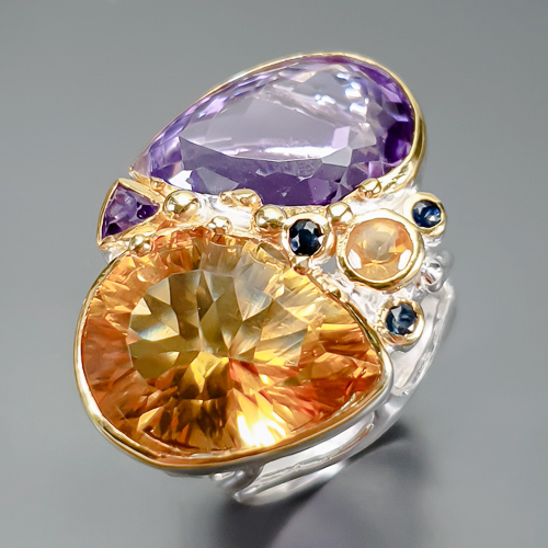 Δαχτυλίδι σε ασήμι 925 με λευκό και κίτρινο επιχρύσωμα στα 14Κ με μοντέρνο σχεδιασμό και 2 πετράδια Κιτρίνη χαλαζία σε σχήμα pear + Round με If-vvs καθαρότητα στα 26,77 ct , δύο Αμέθυστους σε Pear + Trillian κοπή με if  καθαρότητα και βάρος στα 22.95 ct . Το κόσμημα συμπληρώνουν και 3 Ζαφείρια σε round κοπή και βάρος 0.30 ct . Η προέλευση των λίθων είναι απο την Βραζιλία και την Σρι-Λανκα.