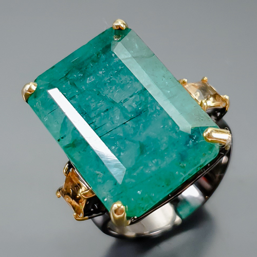 Δαχτυλίδι σε ασήμι 925 με μαύρο και κίτρινο επιχρύσωμα στα 14Κ με Σμαράγδι σε σχήμα octagon με translucent καθαρότητα στα 25.12 ct με έντονο πράσινο χρώμα, Το κόσμημα συμπληρώνουν και 2 πετράδια Κιτρίνη Χαλαζία στα 1.60 ct σε Princess κοπή και Vvs διαφάνεια. Η προέλευση των λίθων είναι απο την Ζάμπια και την Βραζιλία.