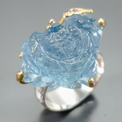 Δαχτυλίδι σε ασήμι 925 με λευκό και κίτρινο επιχρύσωμα στα 14Κ με σκαλιστή Ακουαμαρίνα σκαλισμένη σε σχήμα Λουλουδιού με if-vvs καθαρότητα στα 24.37 ct με έντονο γαλάζιο χρώμα, Το κόσμημα συμπληρώνουν και 5 Αμέθυστοι στα 0.05 ct σε στρογγυλή κοπή και Vvs διαφάνεια. Η προέλευση των λίθων είναι απο την Βραζιλία.